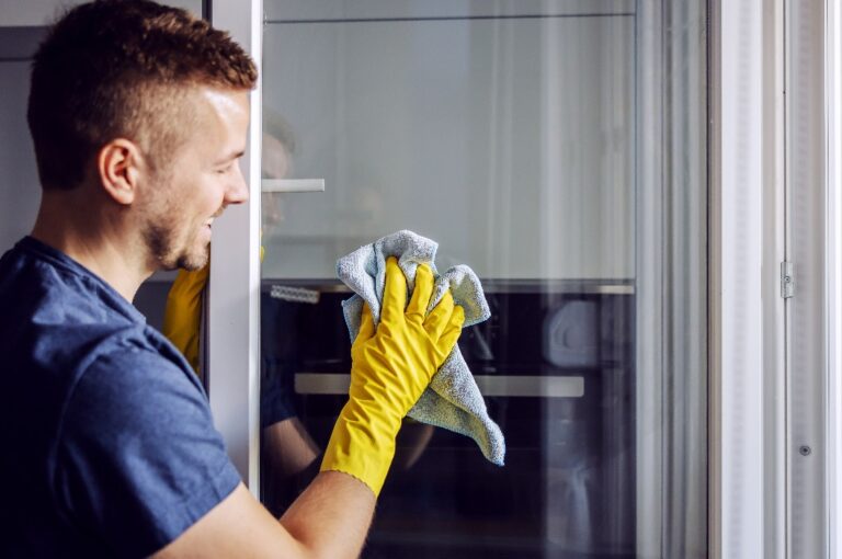 Ein Mann mit Gummihandschuhen putzt mit einem Tuch ein Fenster. Nach dem Regen bleiben immer Flecken auf dem Glas zurück.